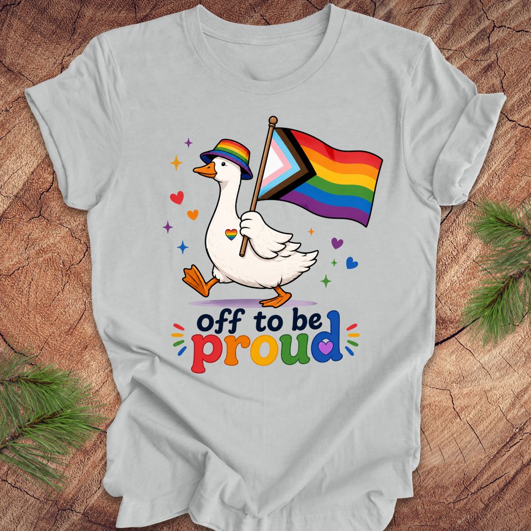 Gray t-shirt with a goose holding a rainbow flag and text 'off to be proud' on a wooden surface.