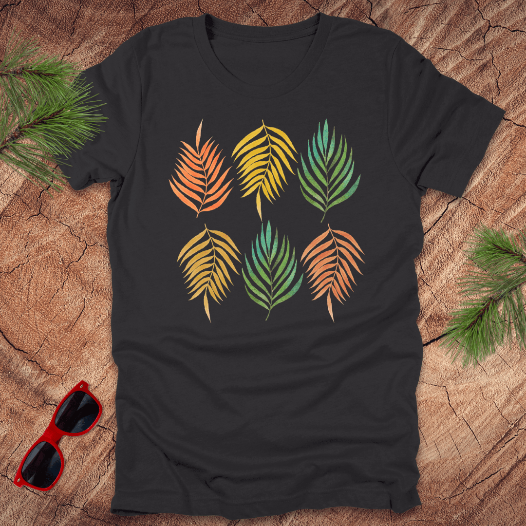 A grey t-shirt with a vibrant leaf pattern in rainbow tones, displayed on a wooden background with foliage accents.