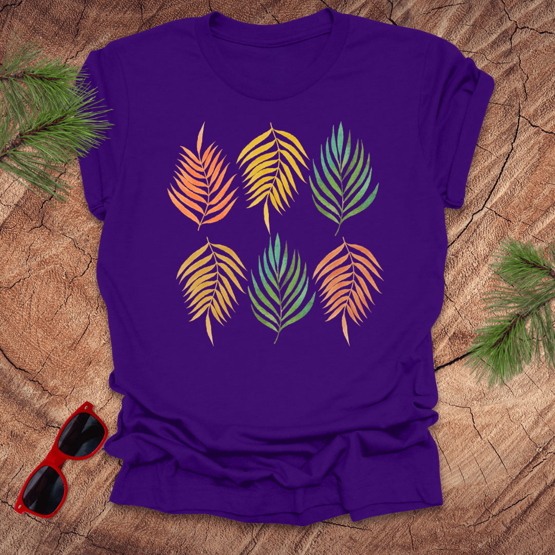 A purple t-shirt with a vibrant leaf pattern in rainbow tones, displayed on a wooden background with foliage accents.
