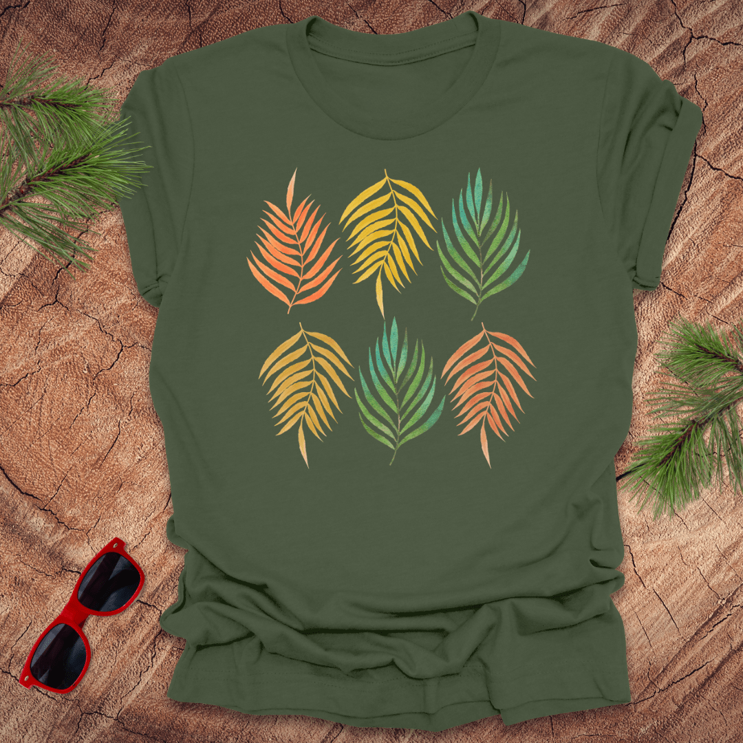 A green t-shirt with a vibrant leaf pattern in rainbow tones, displayed on a wooden background with foliage accents.