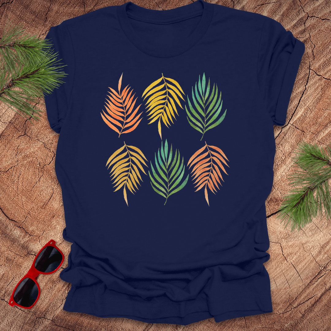 A navy t-shirt with a vibrant leaf pattern in rainbow tones, displayed on a wooden background with foliage accents.