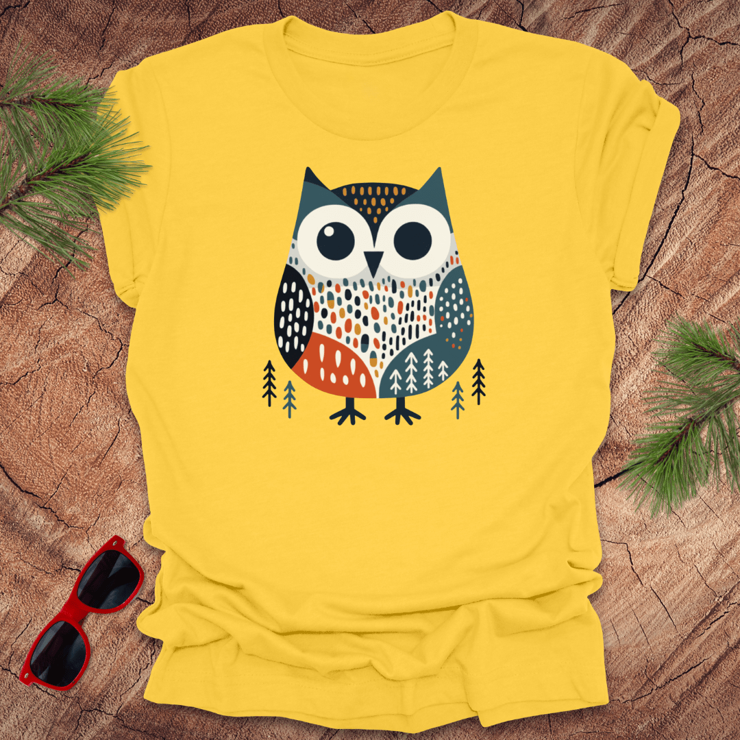 Yellow t-shirt with an owl design on a wooden surface with sunglasses and greenery.