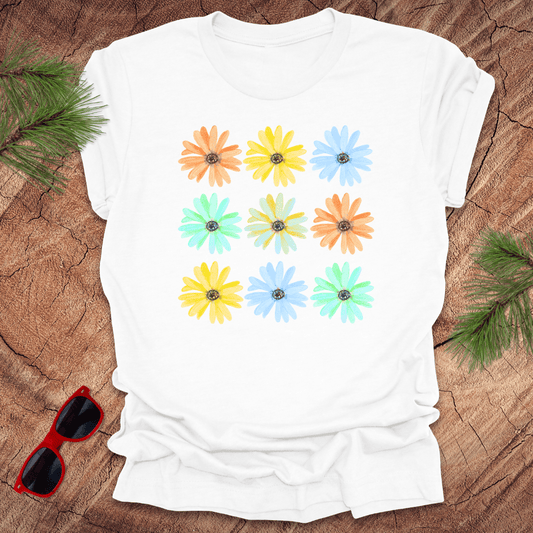 White t-shirt with colorful flower pattern on a wooden surface with sunglasses and greenery.