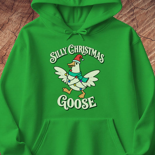 Irish green hoodie with a goose in a Santa hat and teal scarf, wrapped in colorful Christmas lights under retro Silly Christmas Goose lettering, laid flat on a rustic wood background.
