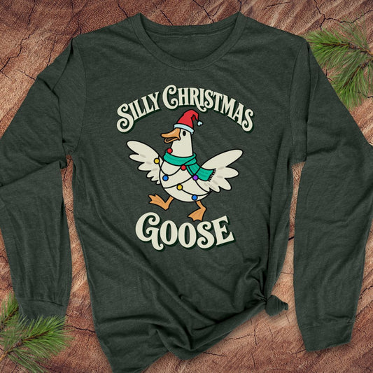Heather forest green long-sleeve t-shirt with a goose in a Santa hat and teal scarf, wrapped in colorful Christmas lights under retro Silly Christmas Goose lettering, laid flat on a rustic wood background with pine branches.