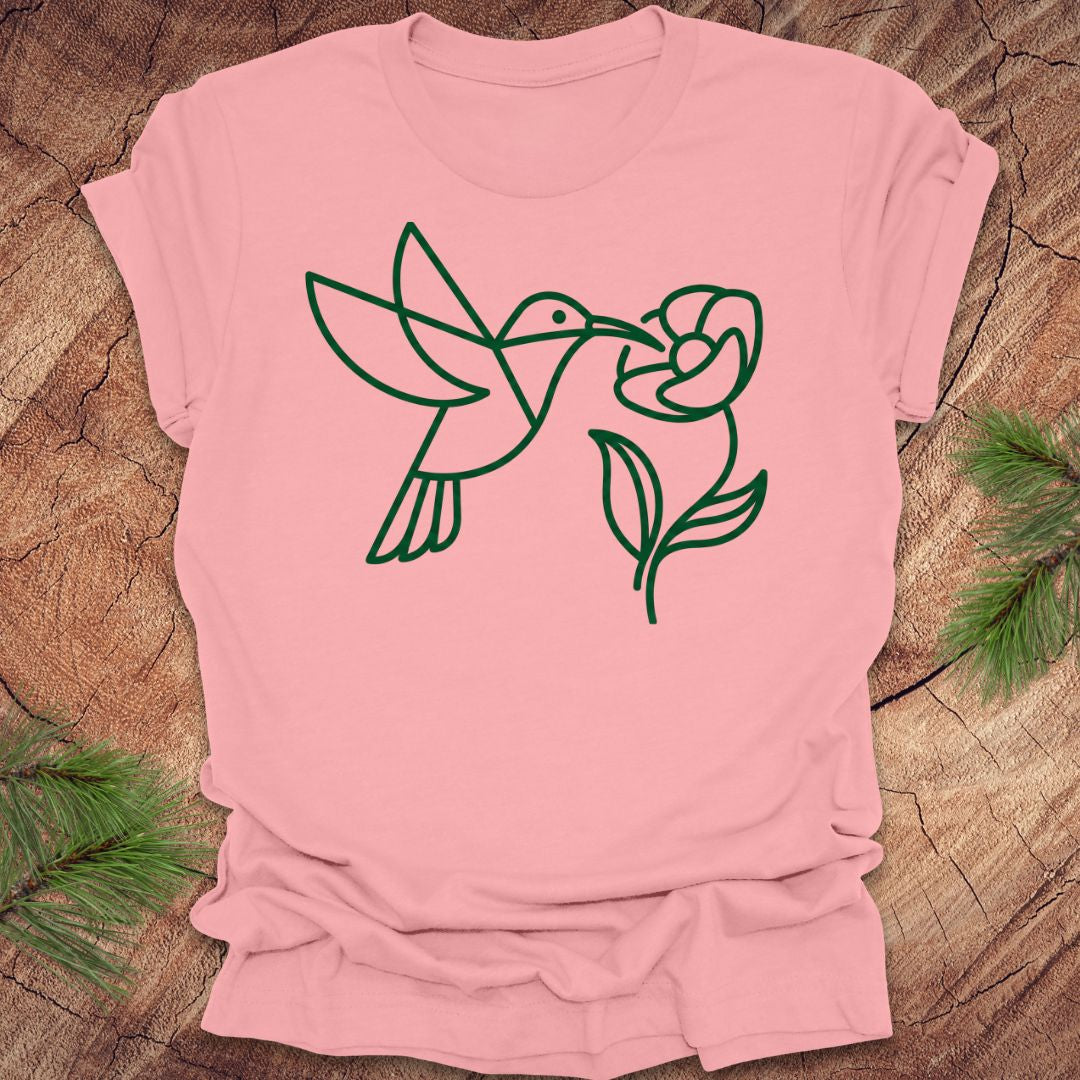Pink t-shirt with green line art of a hummingbird and flower on a wooden surface.