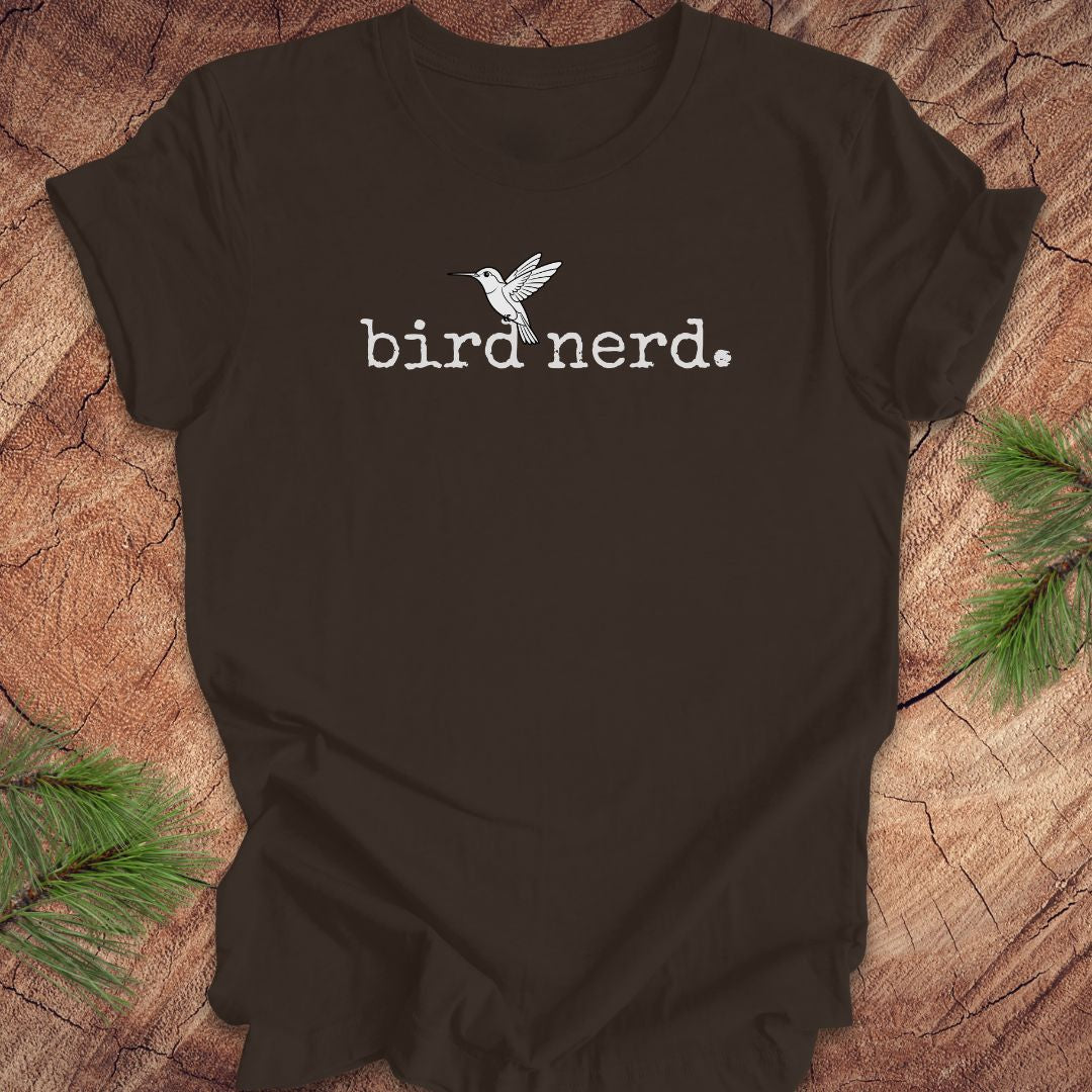 Black t-shirt with 'bird nerd' text and bird graphic on a wooden surface with pine branches.