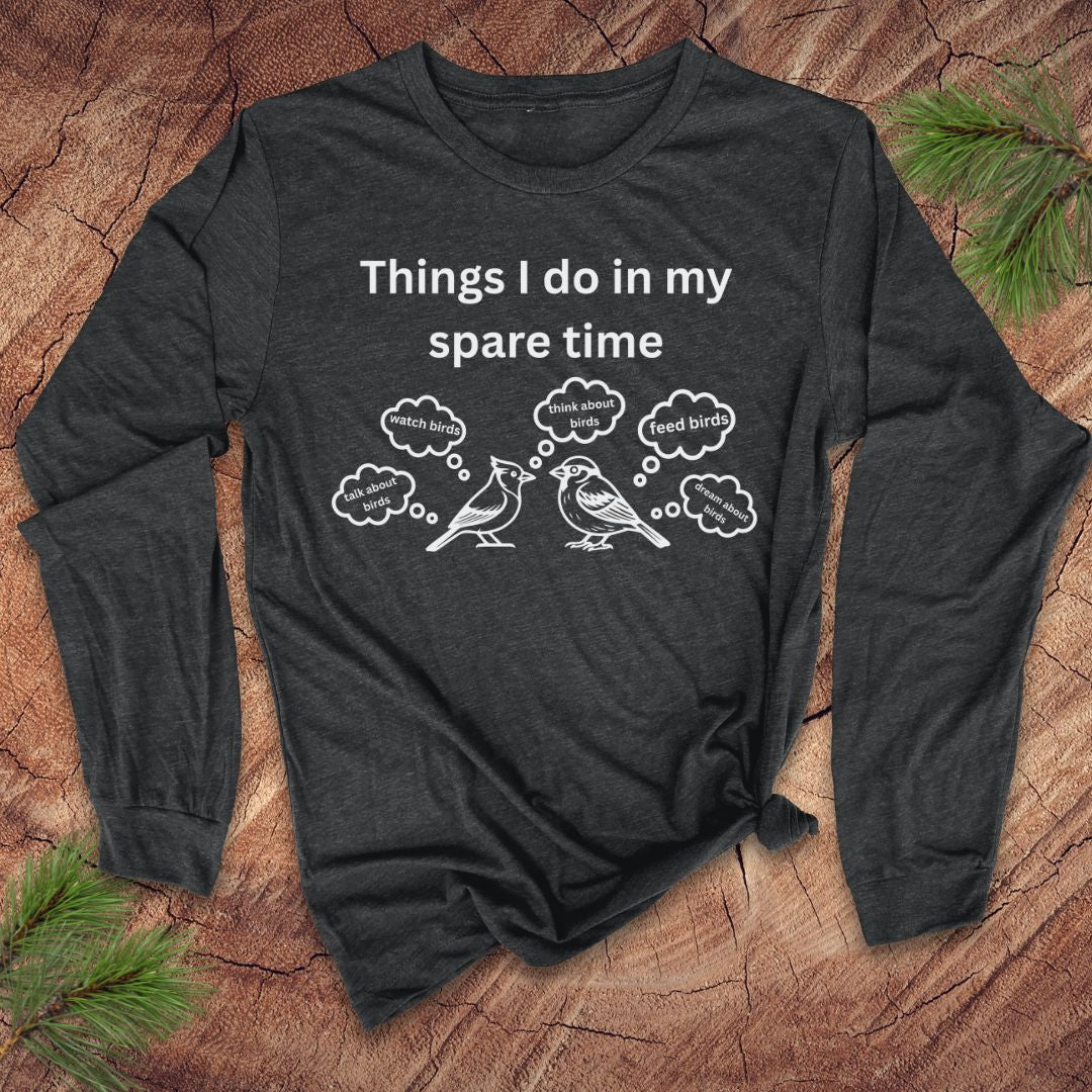 Dark gray long-sleeve tshirt with white text 'things i do in my spare time' with bird graphic and thought bubbles, on a wood surface.
