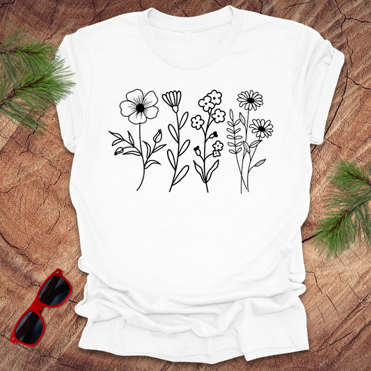 White t-shirt with black floral designs on a wooden surface with sunglasses.