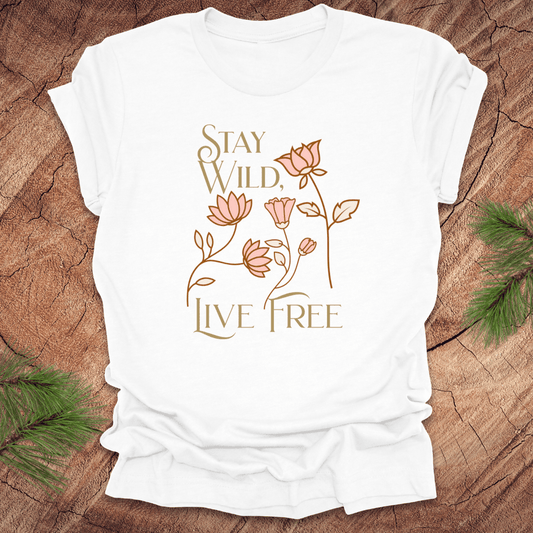 White t-shirt with 'Stay Wild, Live Free' text and floral design on a wooden surface.