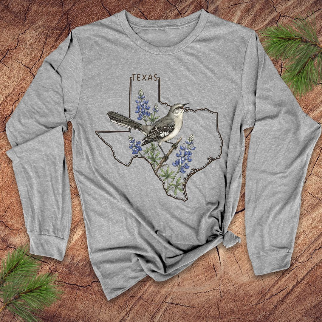 Gray long-sleeve shirt with Texas design featuring a bird and bluebonnets on a wooden surface.