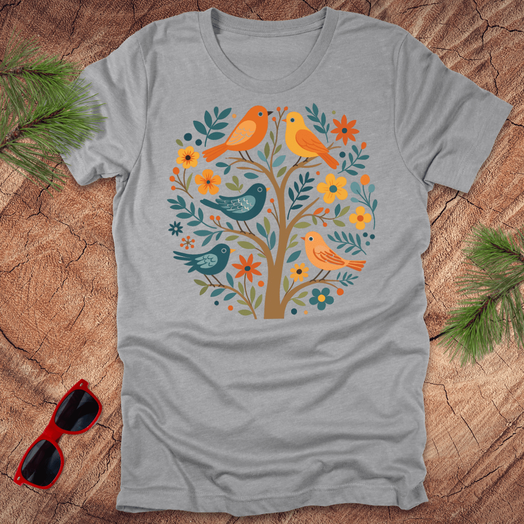 Gray t-shirt with a colorful tree design featuring birds on a wooden surface.