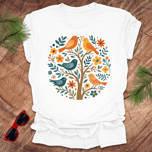 White t-shirt with a colorful bird and floral design on a wooden surface with sunglasses.