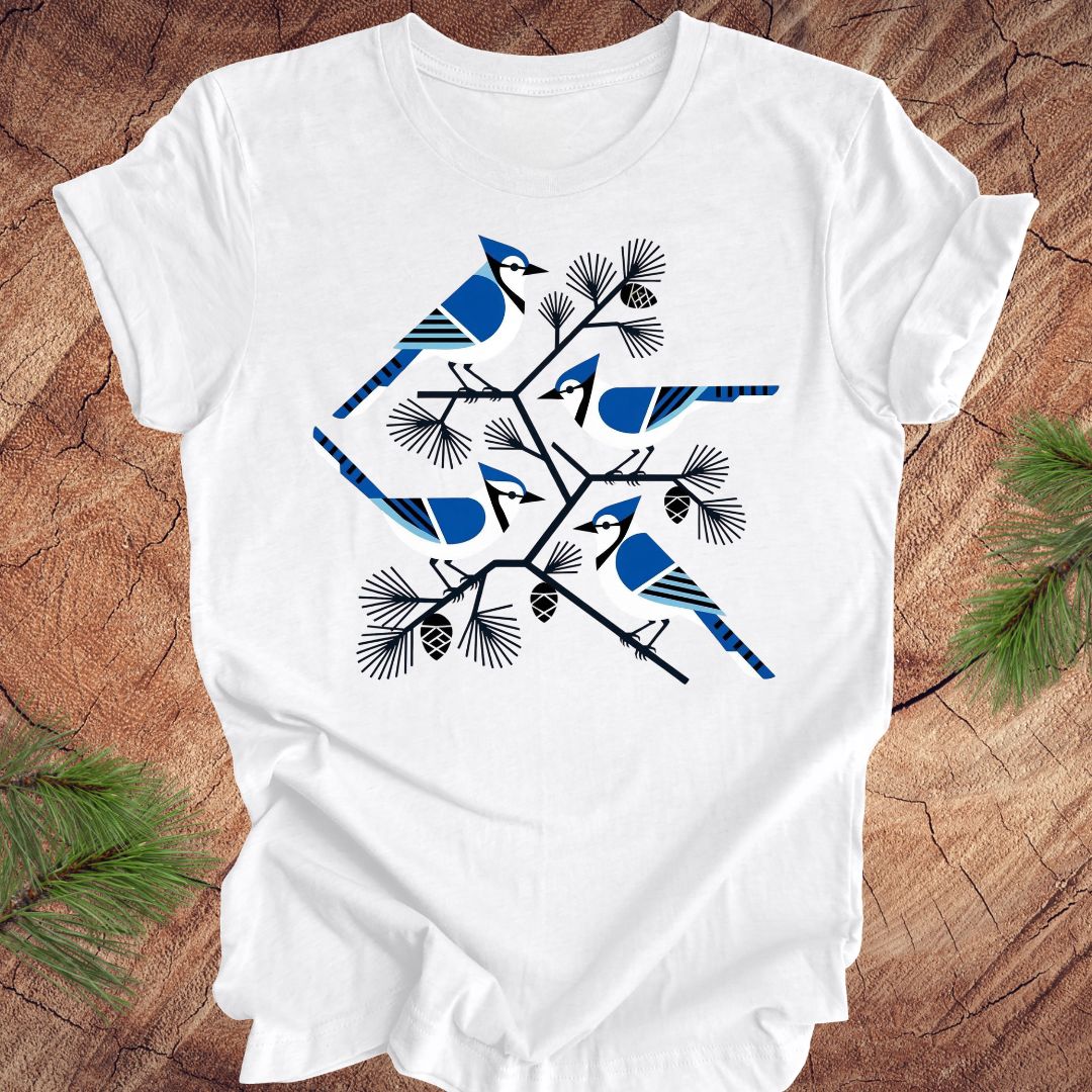White t-shirt with geometric blue jay and tree design, on a wood background.
