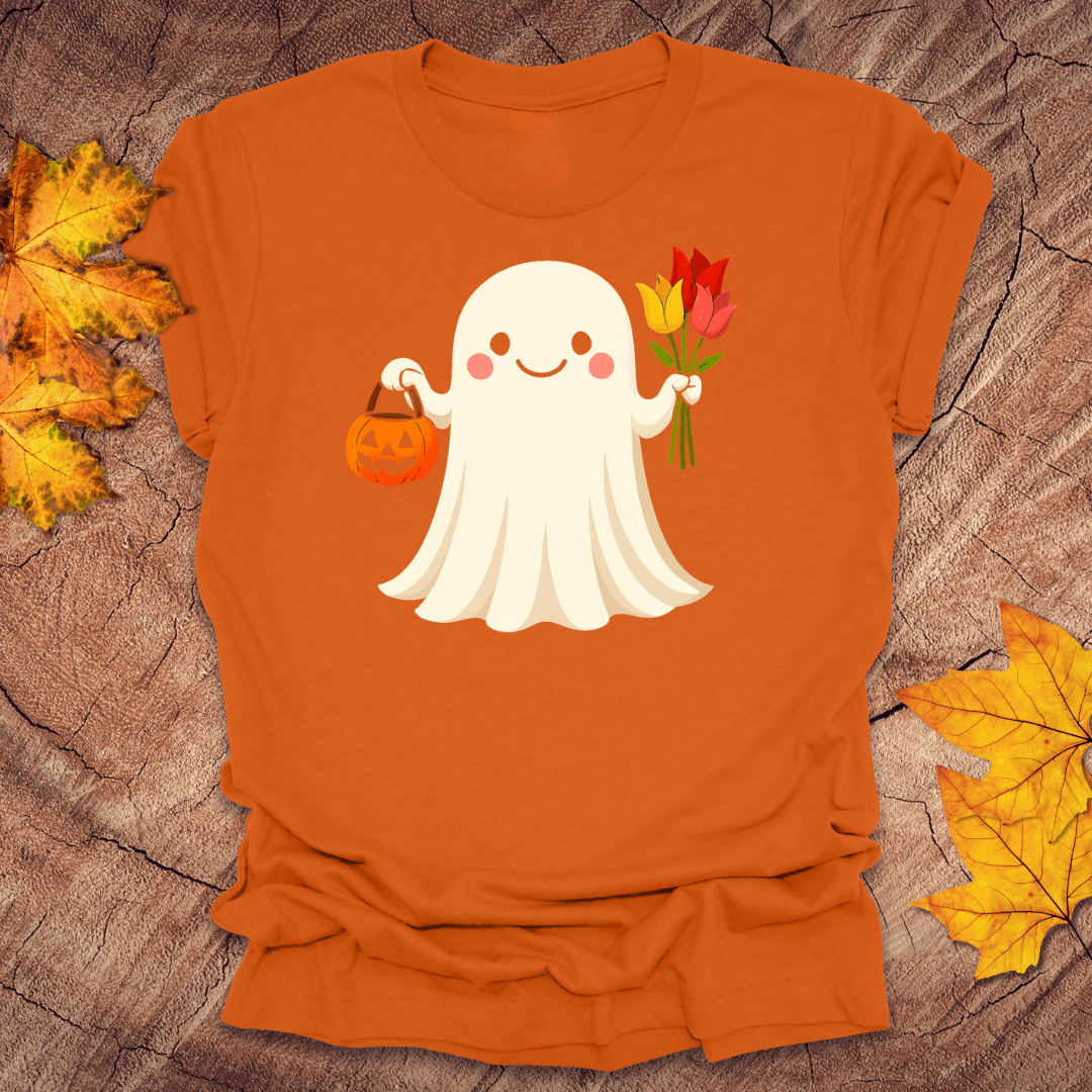 Orange t-shirt with a ghost holding a pumpkin and flowers on a wooden surface with autumn leaves.