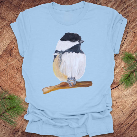 Light blue t-shirt with a chickadee design on a wooden surface