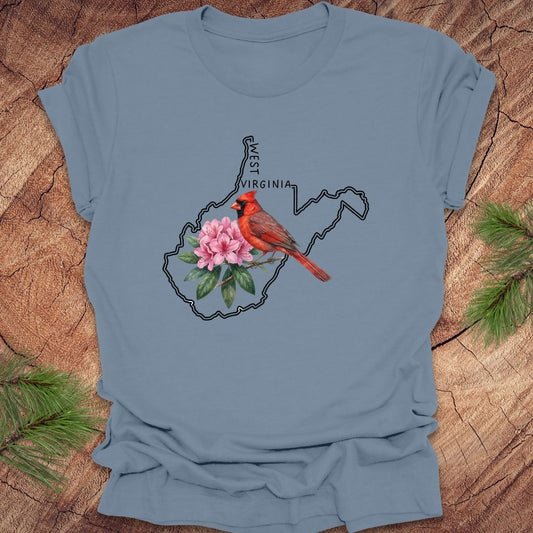 Steel blue t-shirt with the outline of West Virginia and its state bird,and flower cardinal and rhododendron, on a wooden background.