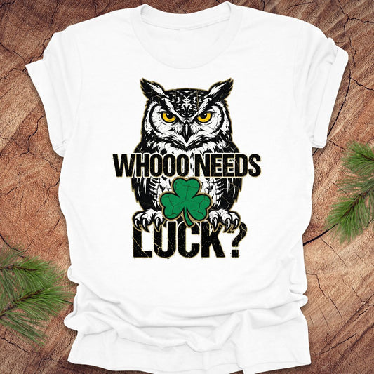 White t-shirt with an owl st patrick's day graphic and text 'WHOO NEEDS LUCK?' on a wooden surface.