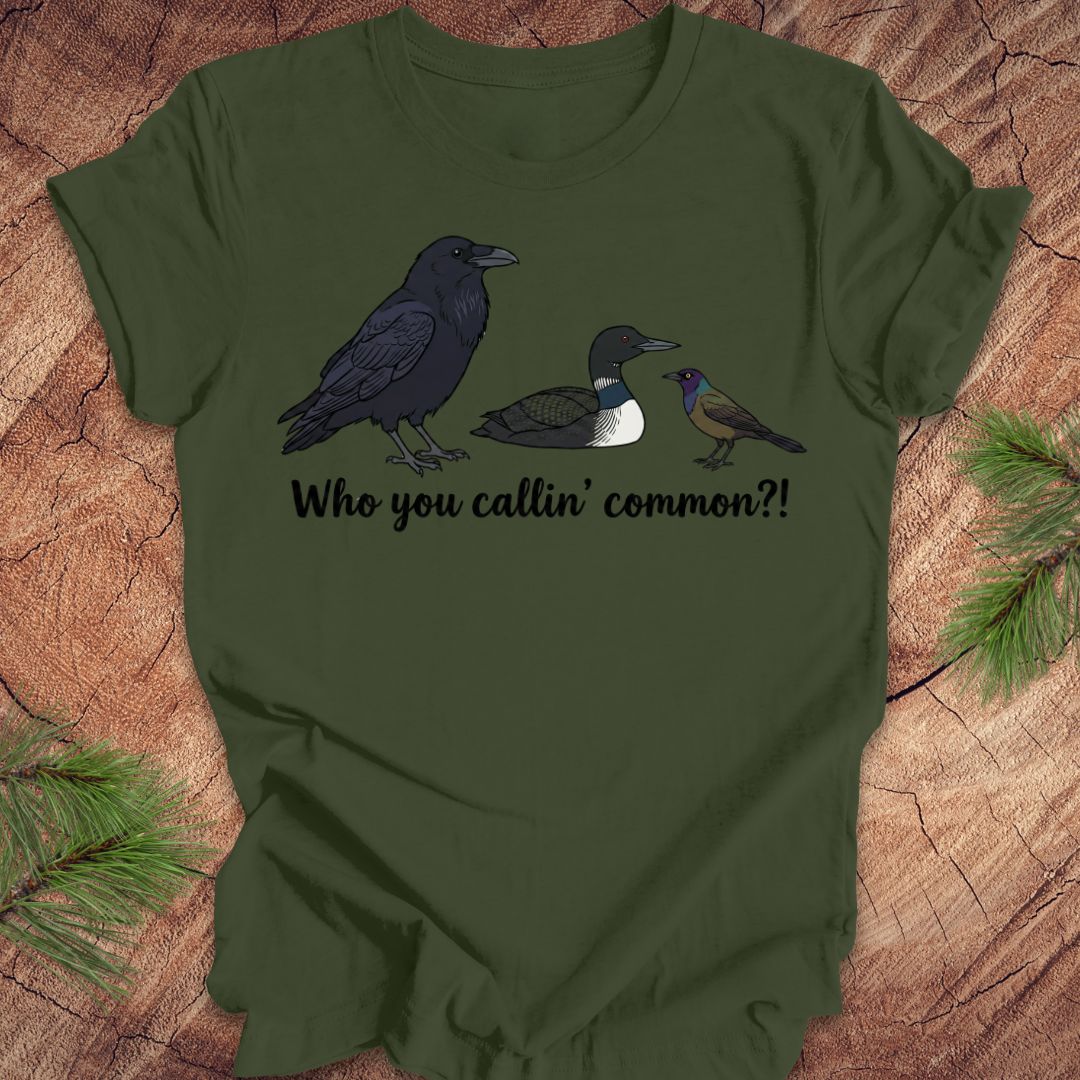 Green t-shirt with bird illustrations and text on a wooden surface