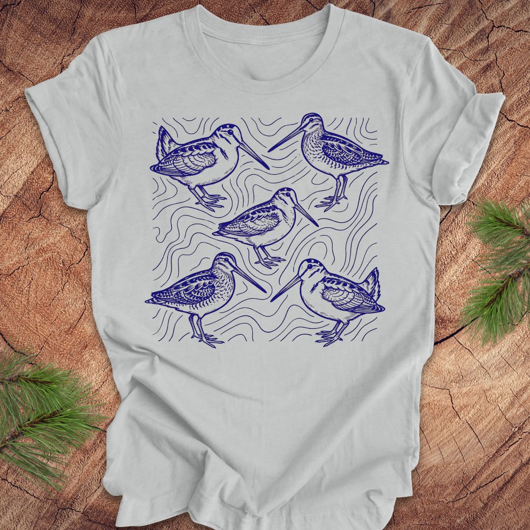 Silver t-shirt with blue woodcock and wilson's snipe bird illustrations on a wooden surface