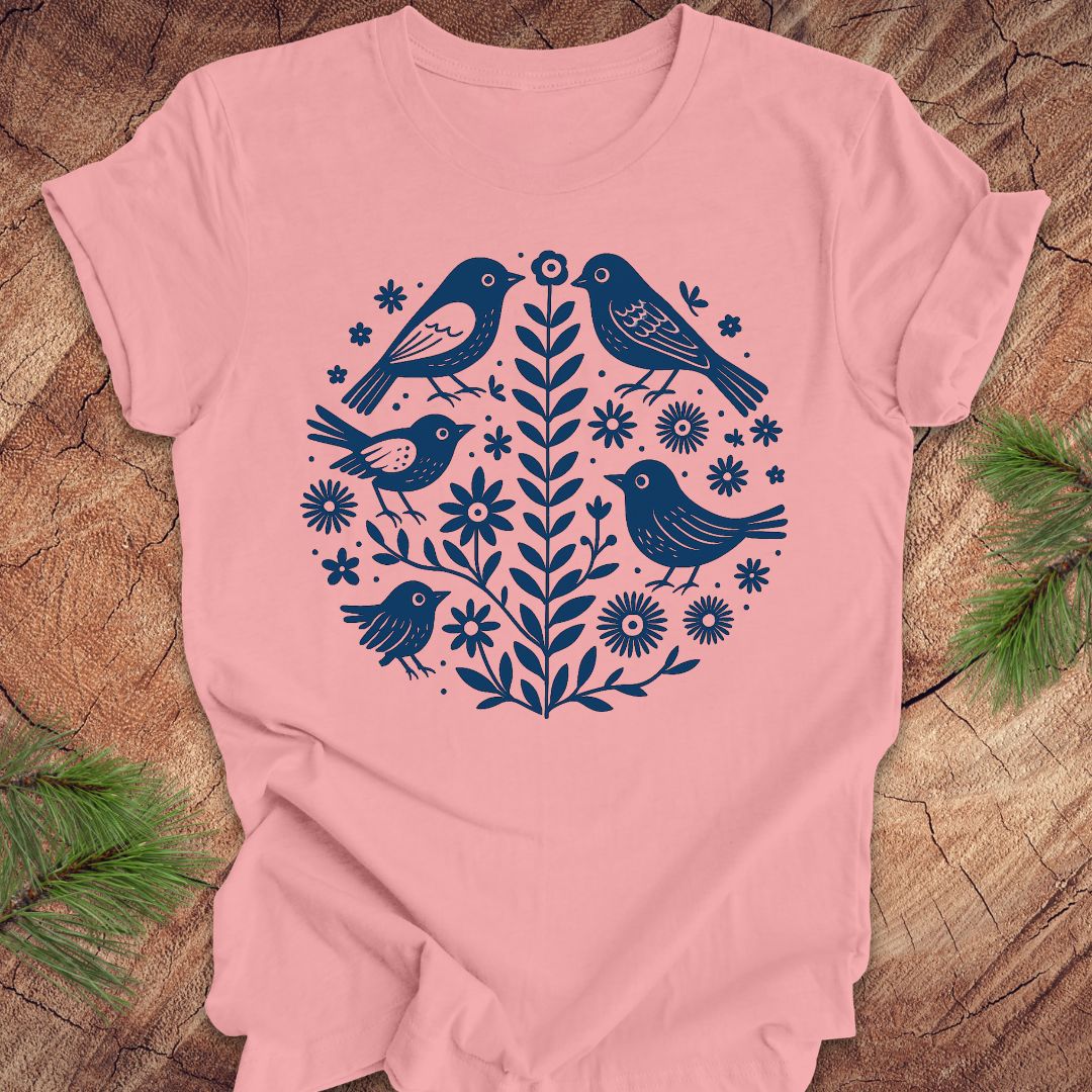 Pink t-shirt with folk art blue bird and floral design on a wooden surface
