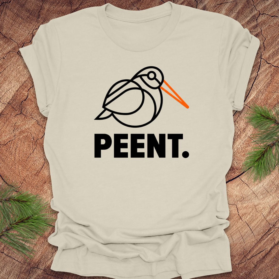 Beige t-shirt with a woodcock graphic and 'PEENT.' text on a wooden surface.