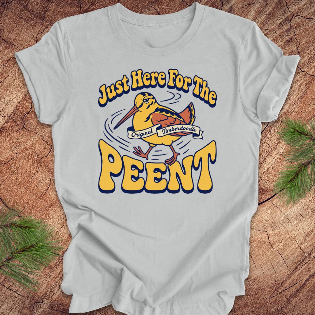 Gray t-shirt with 'Just Here For The Peent' woodcock graphic on a wooden surface