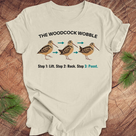 Beige t-shirt with woodcock wobble graphic and text on a wooden surface