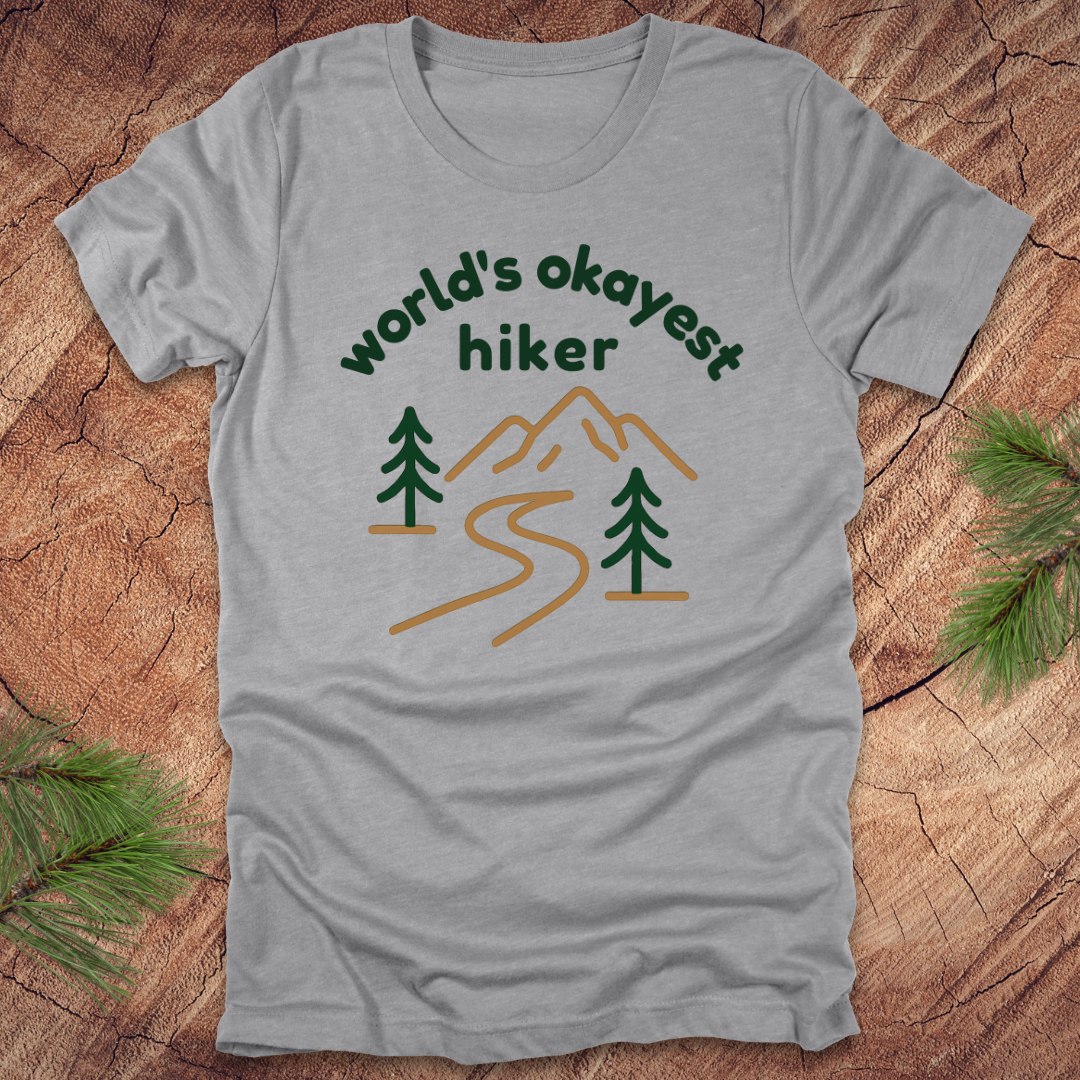 Gray t-shirt with 'world's okayest hiker' graphic on a wooden surface