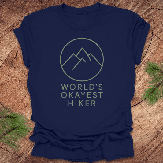 Navy blue t-shirt with 'World's Okayest Hiker' text and mountain graphic on a wooden surface.