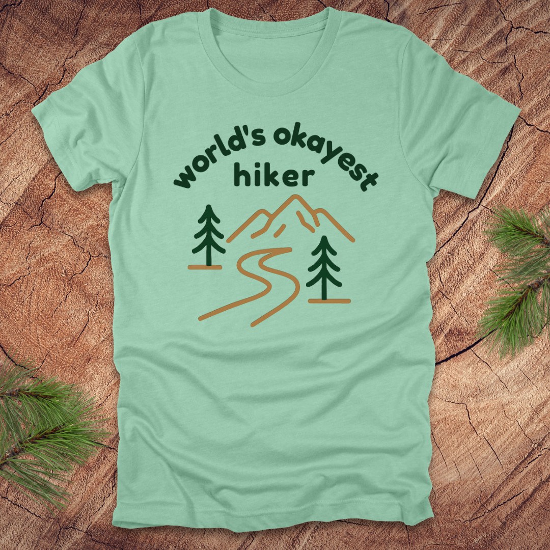 Light green t-shirt with 'world's okayest hiker' graphic on a wooden surface