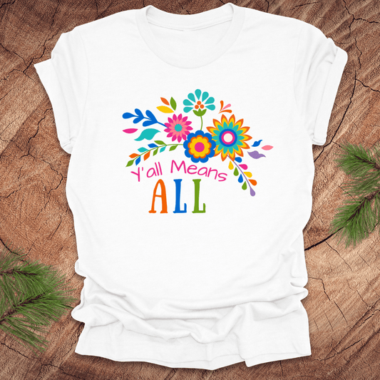 White t-shirt with colorful floral design and text 'Y'all Means All' on a wooden surface