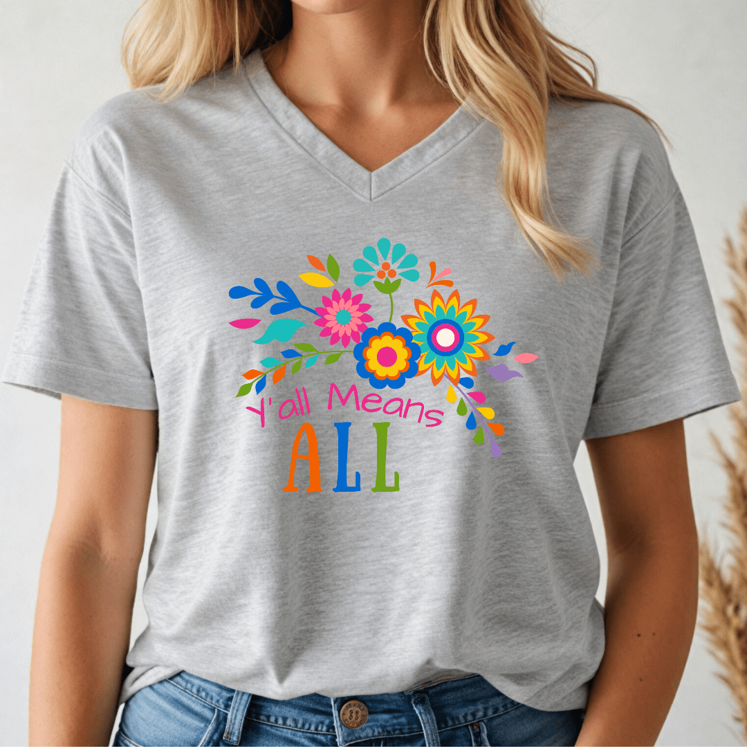 Person wearing a gray v-neck t-shirt with colorful floral design and text, 'Y'all Means All'.