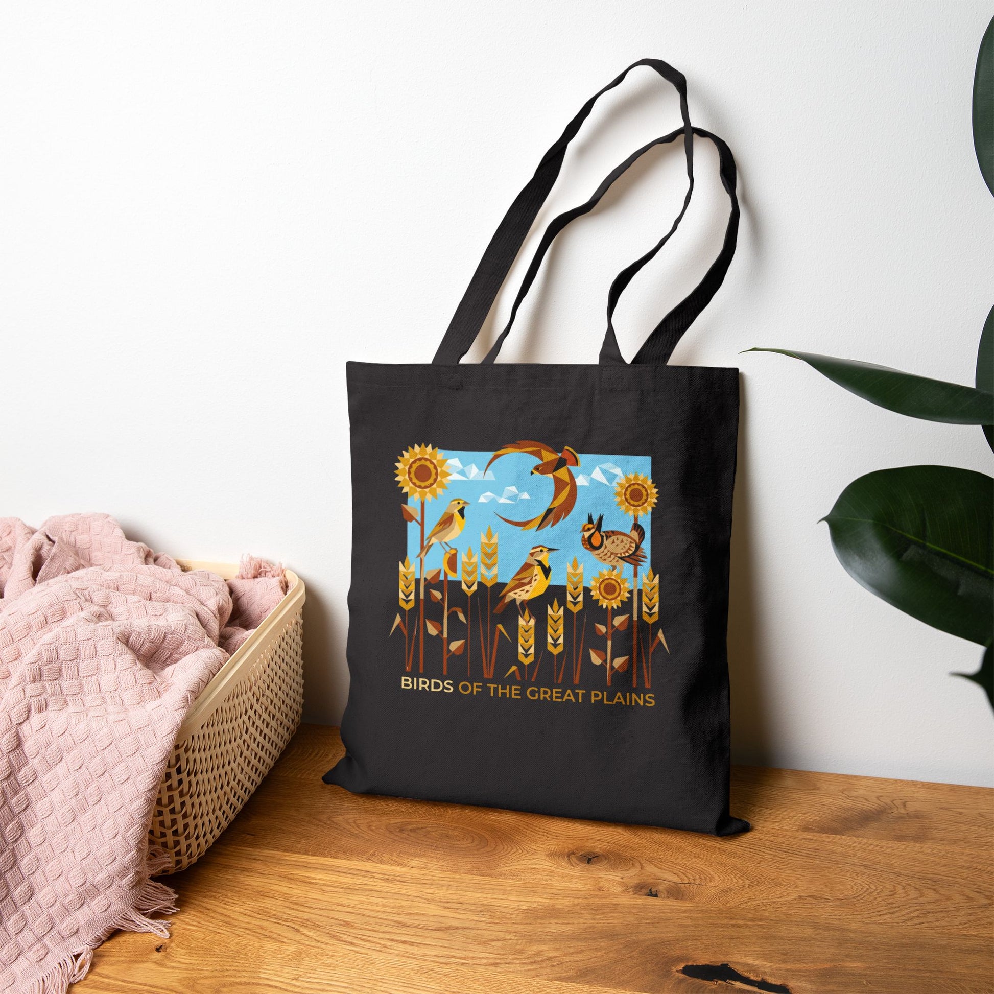 Black tote bag with 'Birds of the Great Plains' design on a wooden surface.