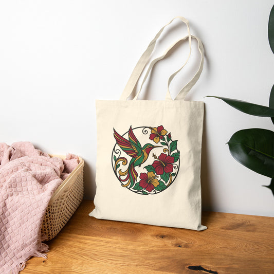 Beige tote bag with a colorful hummingbird and floral design on a wooden surface.