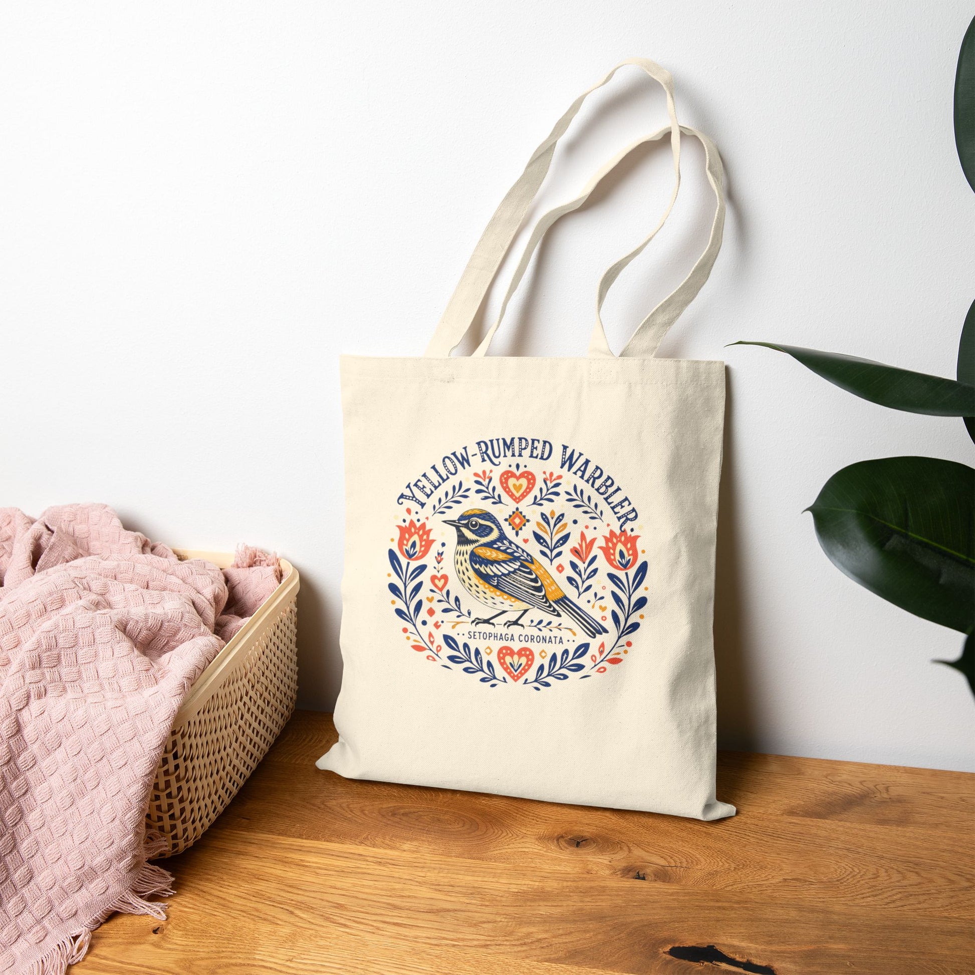Canvas tote bag with a folk art yellow-rumped warbler design on a wood table.