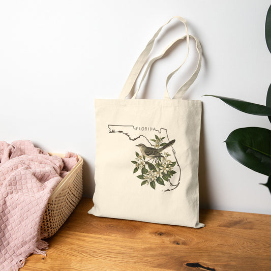 Tote bag with Florida bird design on a wooden surface next to a basket and plant