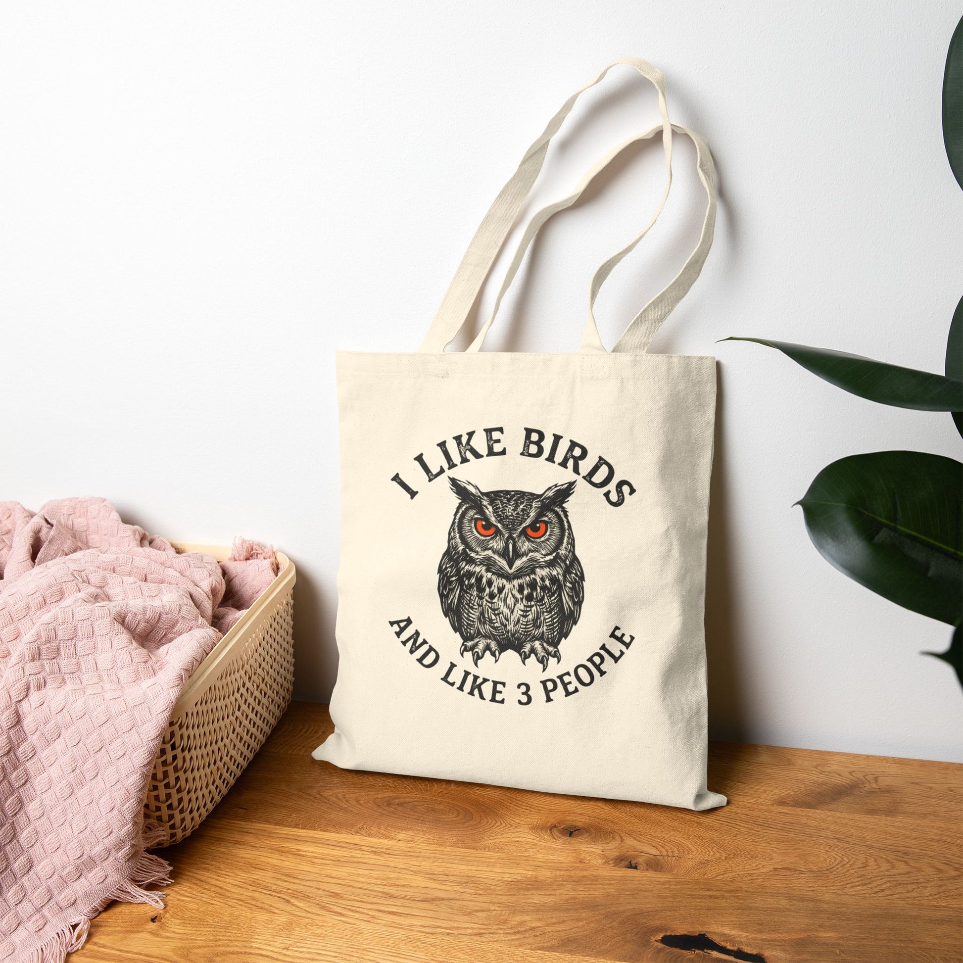 Tote bag with owl design and text on a wooden surface with a white wall background