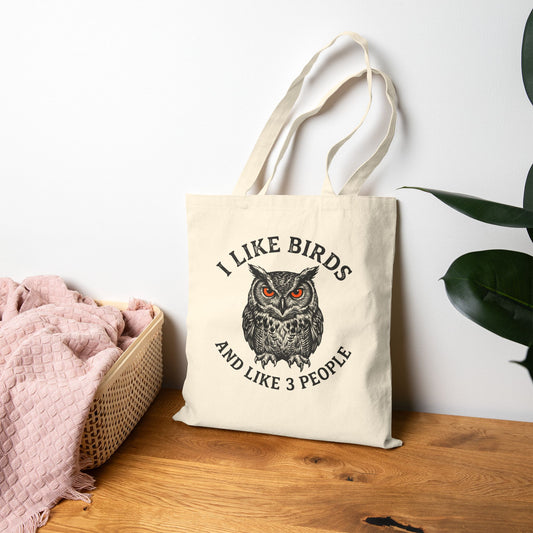 Tote bag with owl design and text on a wooden surface with a white wall background