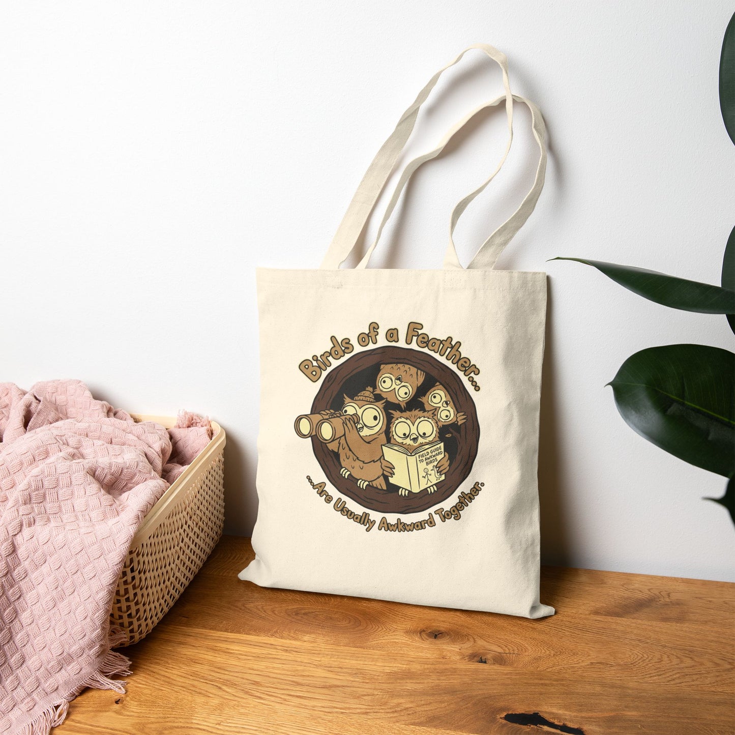 Tote bag with owl design and text on a wooden surface with a white wall background