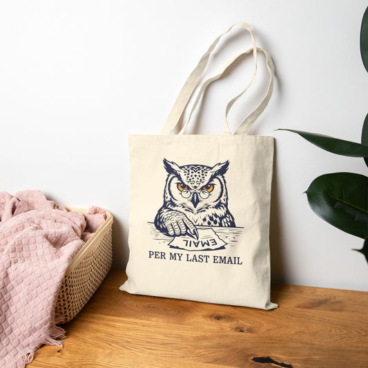 Tote bag with owl design and text on a wooden surface with a white wall background