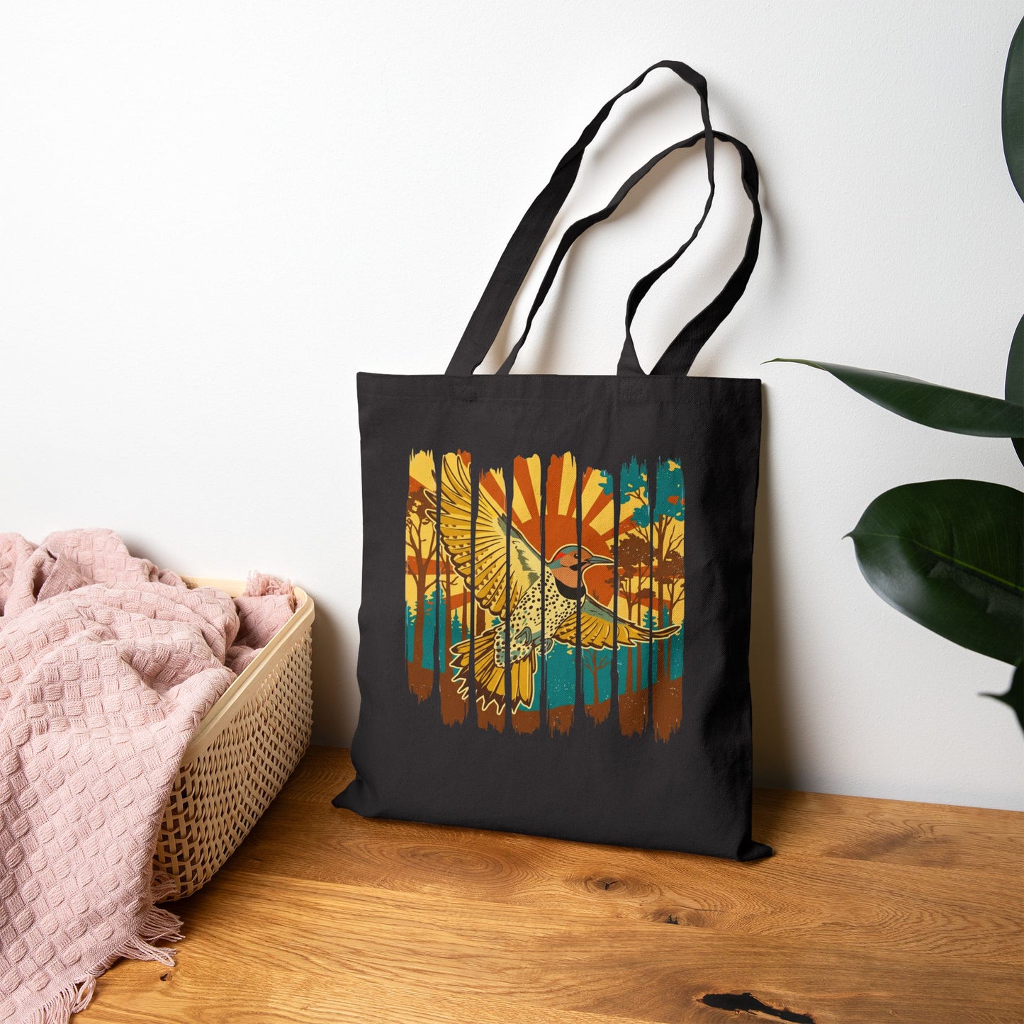 Black tote bag with a colorful bird design on a wooden surface with a white wall background