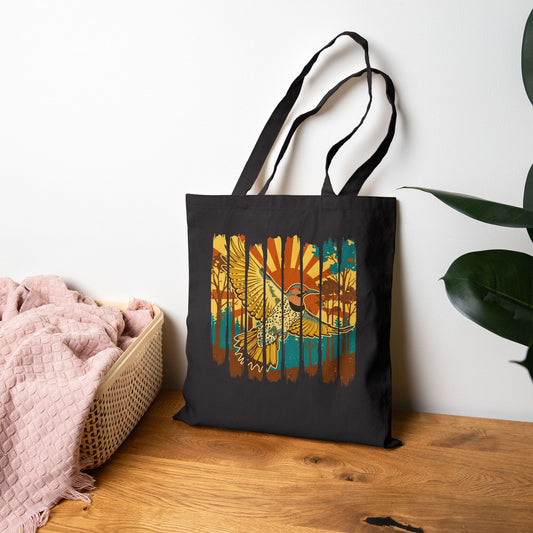 Black tote bag with a colorful bird design on a wooden surface with a white wall background