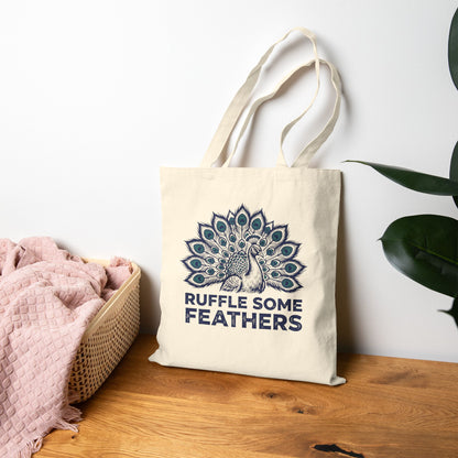 Tote bag with peacock design and 'Ruffle Some Feathers' text on a wooden surface.
