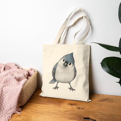 Beige tote bag with a titmouse design on a wooden surface with a white wall and plant in the background