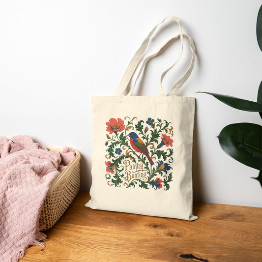 Tote bag with floral and painted bunting bird design on a wooden surface with a white wall background