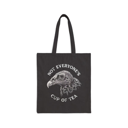 A black canvas tote bag with two black handles, featuring a white graphic of a vulture's head with the text 'NOT EVERYONE'S CUP OF TEA' printed around it, shown against a plain white background.