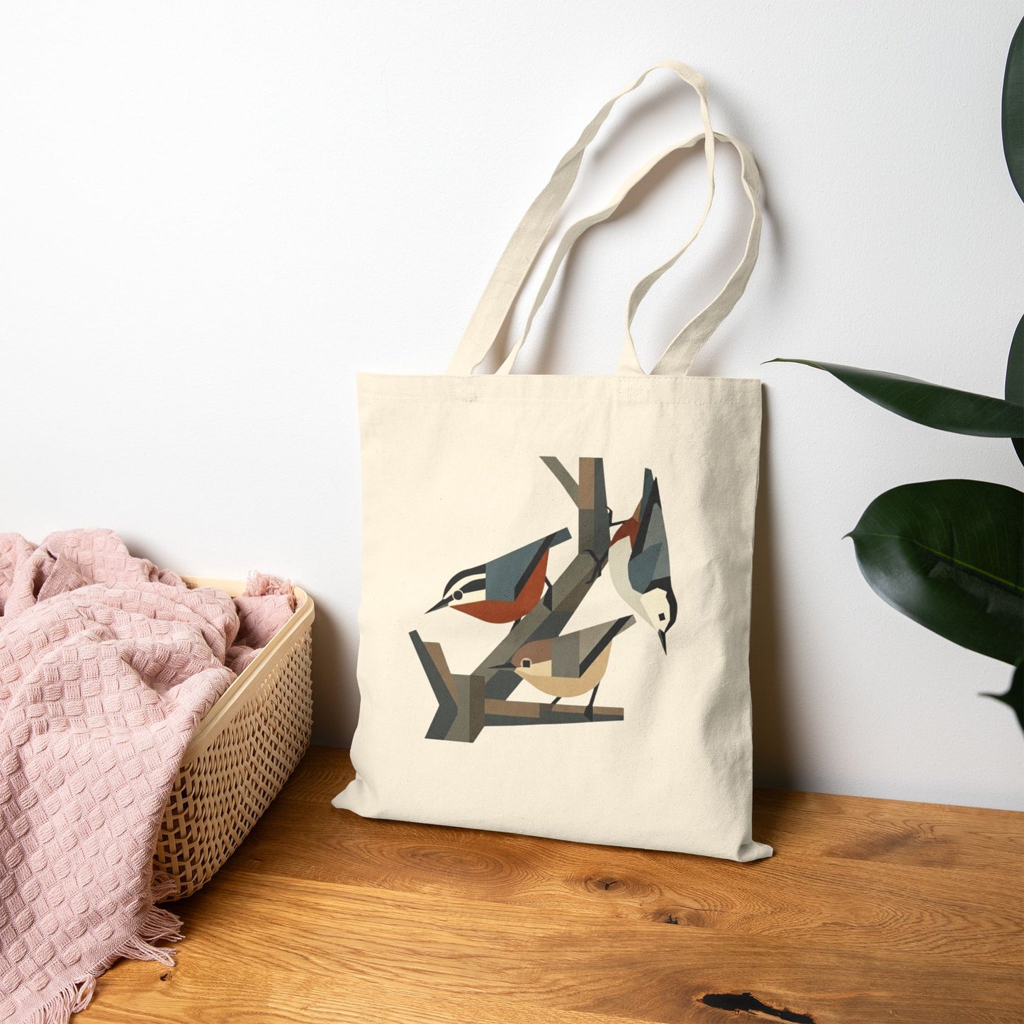 Tote bag with nuthatch design on a wooden surface next to a pink blanket and plant