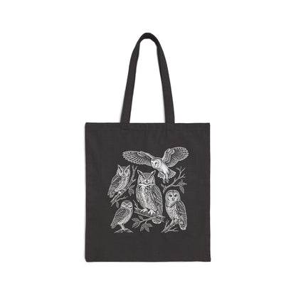 A black canvas tote bag with two shoulder straps, featuring a detailed white line art illustration of five owls perched on branches on the front, set against a plain white background.