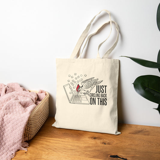 Tote bag with a woodpecker design and text on a wooden surface with a white wall background